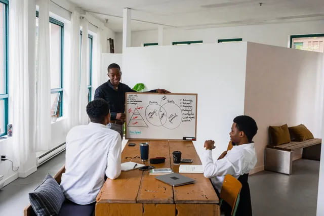 Three men engage in a business meeting with a whiteboard in a modern office. Social media agency rollout planning for client teams