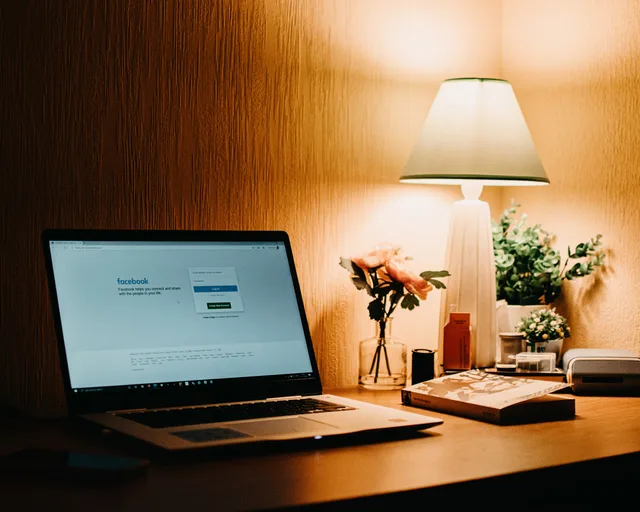 Warmly lit workspace featuring a laptop open to Facebook, a lamp, and decorative items. UK rules and ethics for a social media agency